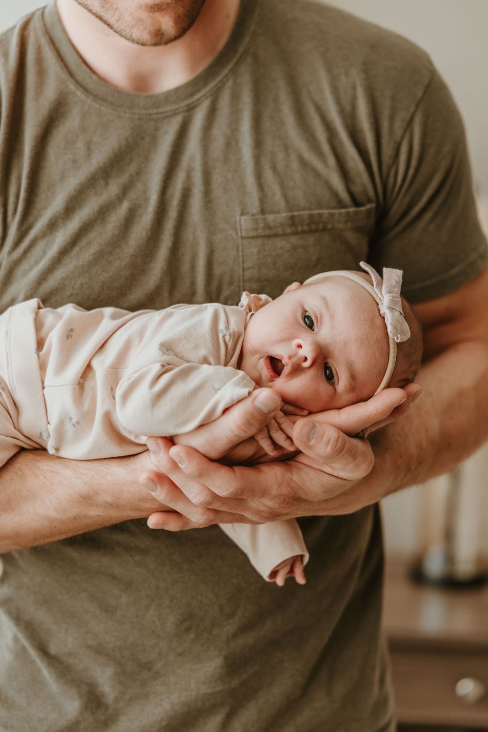 A gentle moment captured in soft light shows a baby being cradled while wearing a light-colored onesie.