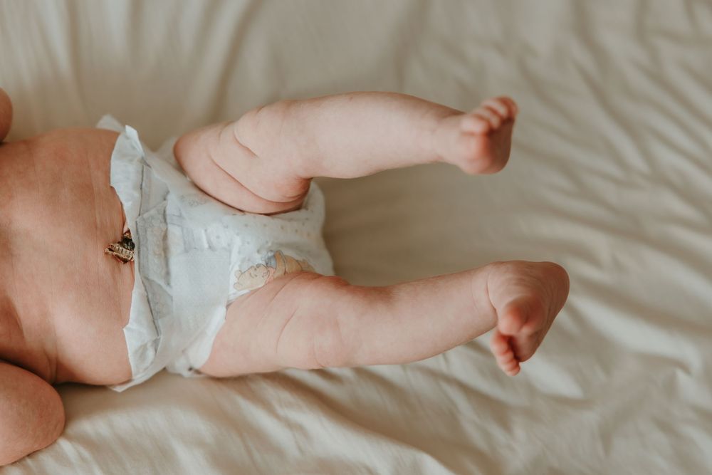 Close up view of baby legs wearing white diaper lying on soft white bedding.