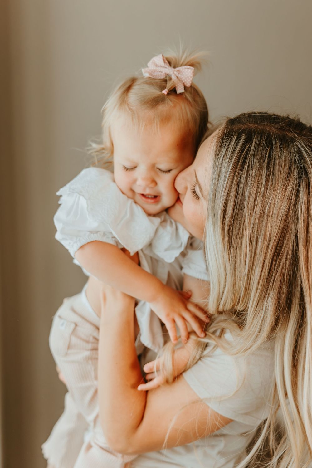 A tender motherhood moment shows playful affection and joy while wearing matching white outfits in warm lighting.