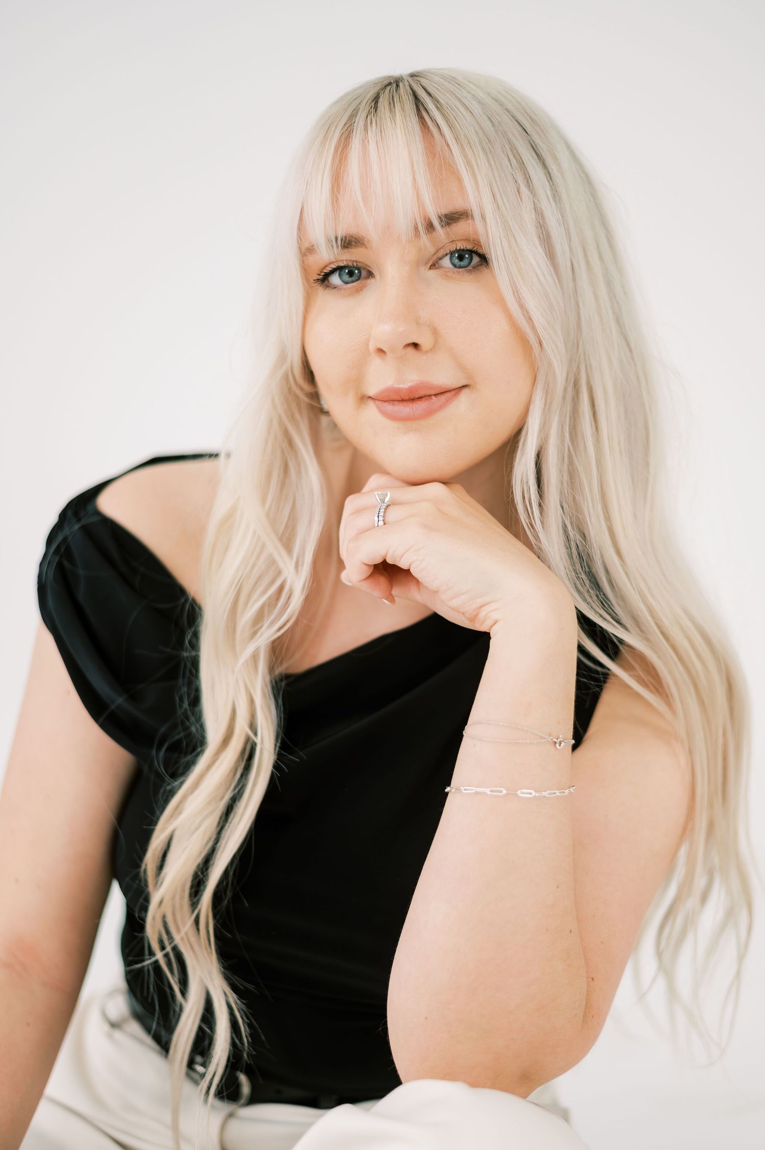 A fashion model wearing a black sleeveless top and white high-waisted pants poses against a white backdrop.