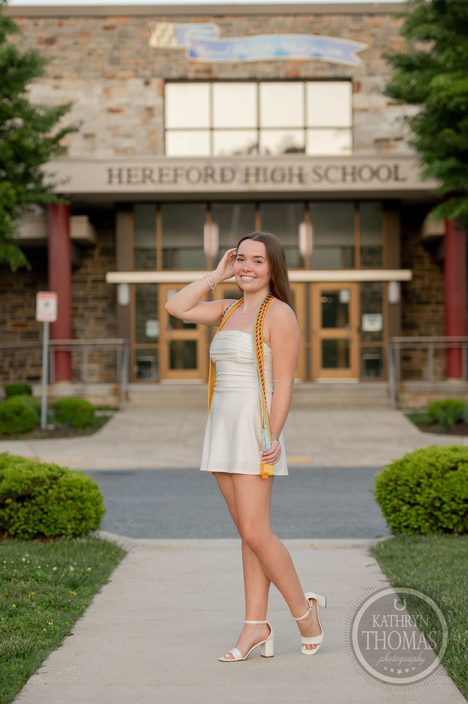 A white summer dress and heels stand out against the stone facade of Hereford High School on a sunny day.