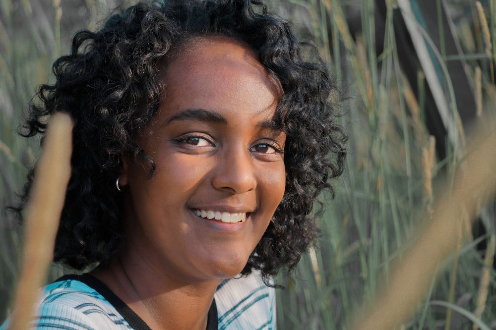 Portrait of high school senior smiling in natural light, framed by tall grass during outdoor session