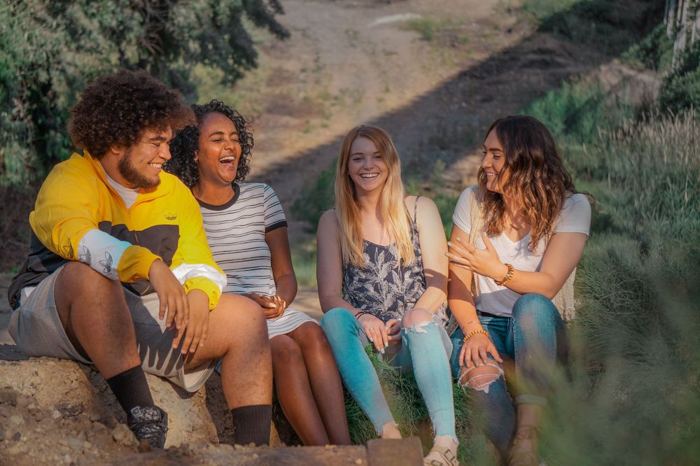 Group of friends laughing and sitting on a dirt path during golden-hour lifestyle photo session