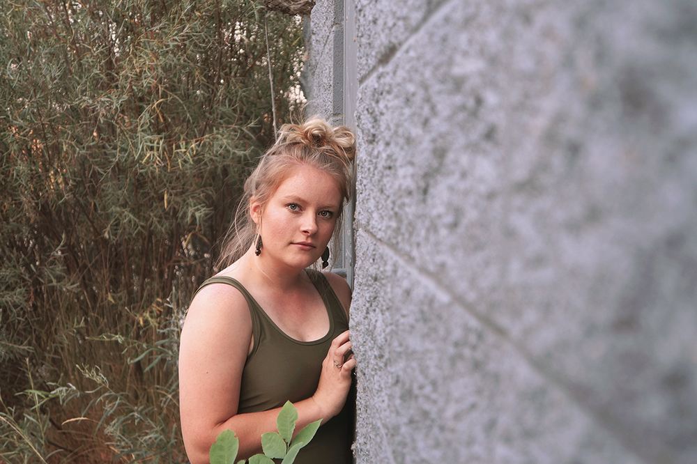 Teen girl smiling in front of a textured wall during an outdoor Senior Portrait session in Tri-Cities WA