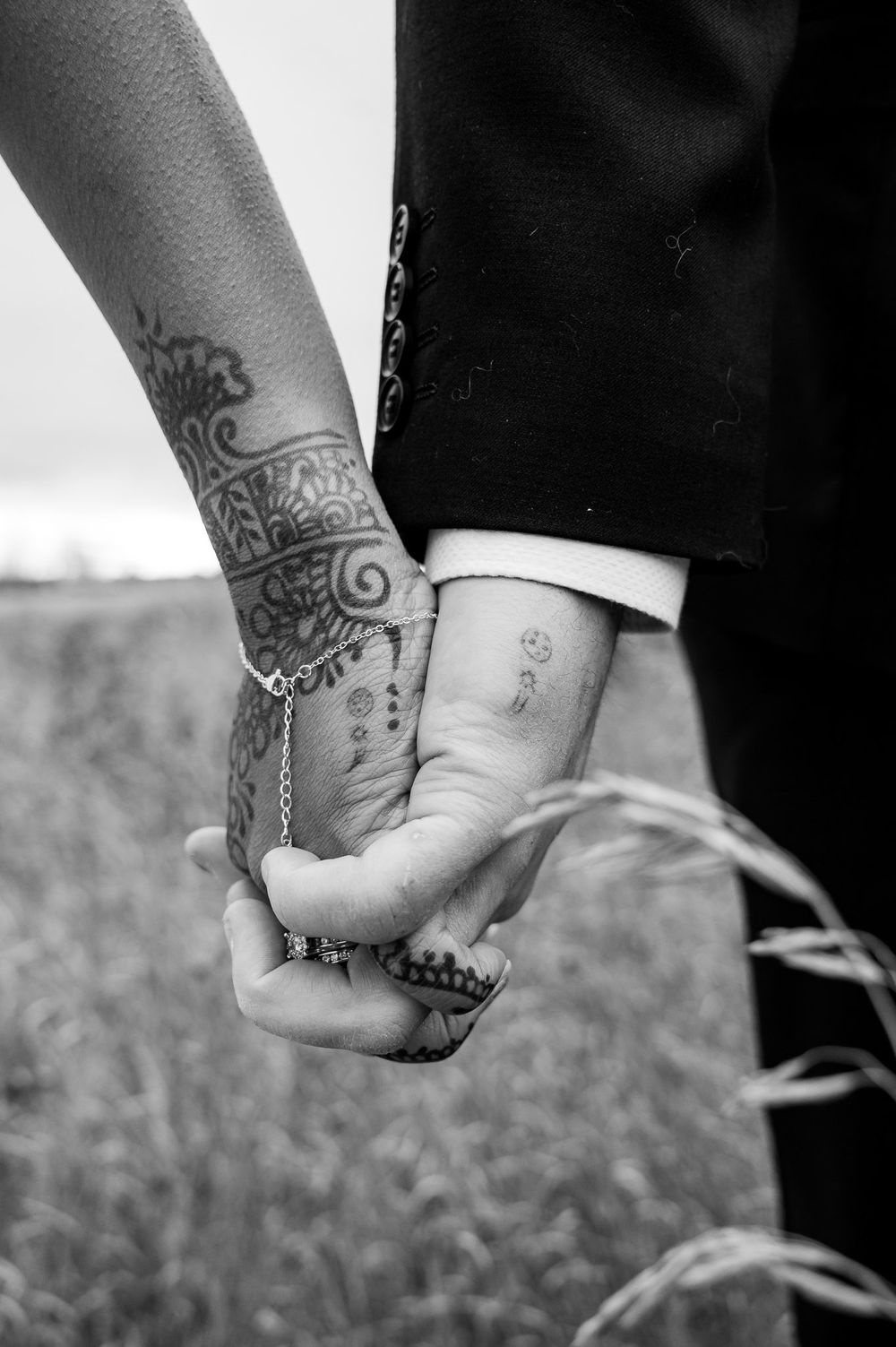 Close-up of two hands with henna tattoos holding each other against a dark background.