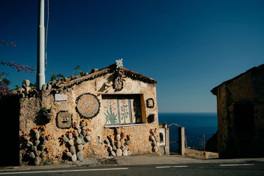 A scenic coastal road winds along rugged cliffs overlooking the Mediterranean Sea on a sunny day.