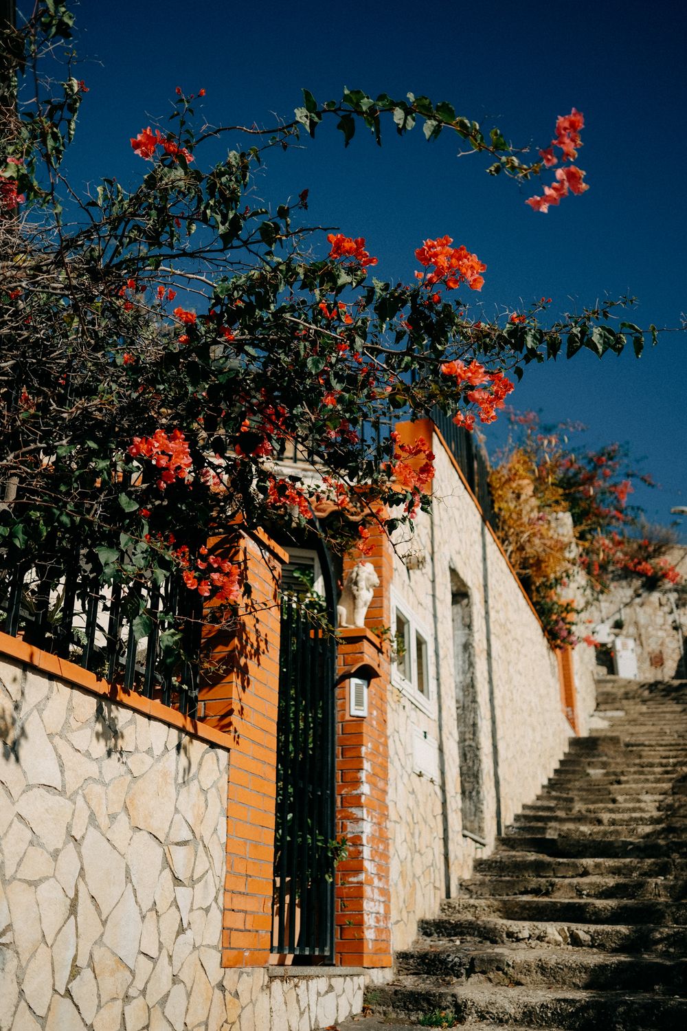 Stone steps with orange brick walls and red flowering bougainvillea against deep blue sky create a Mediterranean atmosphere.