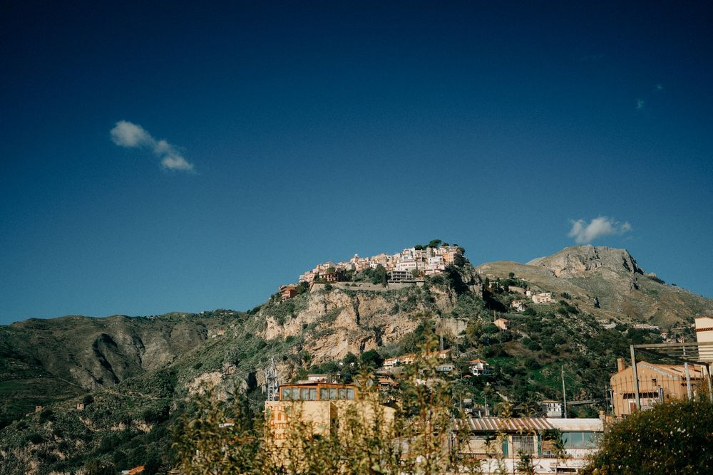 A scenic panoramic view of a coastal town nestled between mountains and blue sea under bright sunny skies.