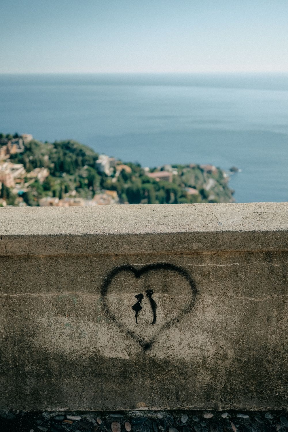 A heart symbol spray painted on a concrete wall overlooking a coastal Mediterranean town and blue ocean view.