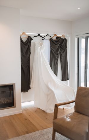 Wedding dresses and formal attire hanging on display in a modern room with hardwood floors and white walls.