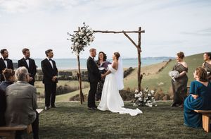 Outdoor hilltop wedding ceremony with rustic wooden arch and mountain views in background.