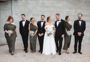 Wedding party lined up against concrete wall posing for creative group photo.