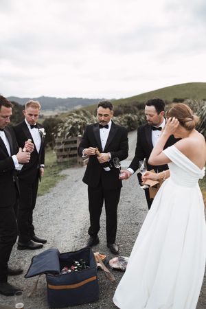 Wedding party gathered on a gravel path sharing champagne during outdoor celebration.
