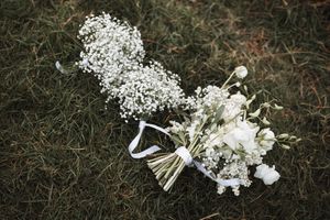 Delicate white baby's breath flowers and wedding bouquet details laid on grass.