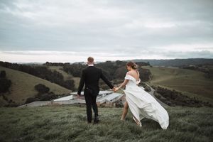 Dramatic wedding photography on rolling hills with flowing white dress and scenic coastal landscape.