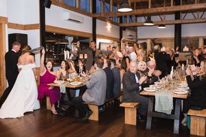 Wedding reception in rustic wooden barn venue with guests seated at long tables.