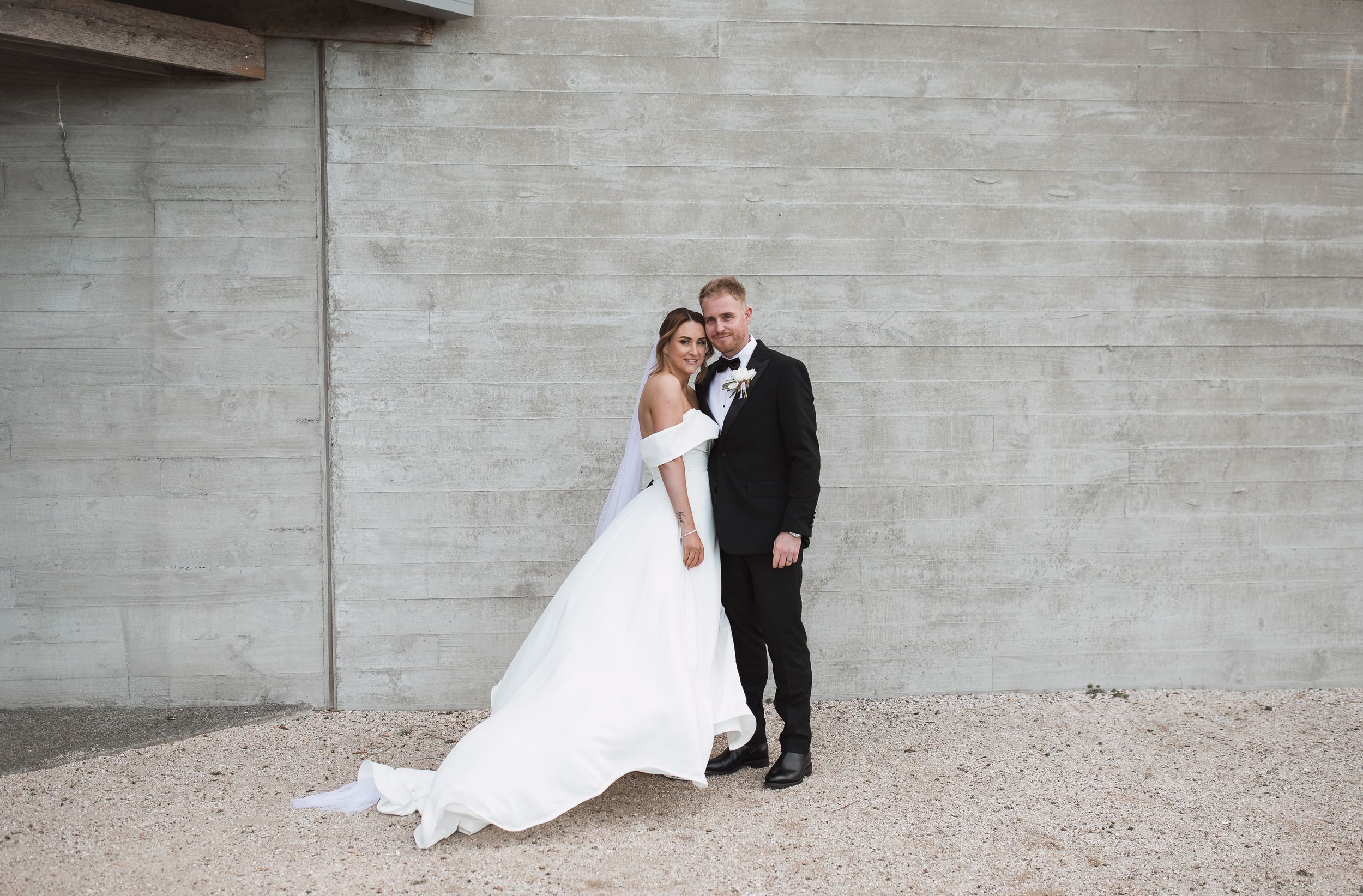A couple in wedding attire poses for romantic photos against a concrete wall in a series of candid shots.