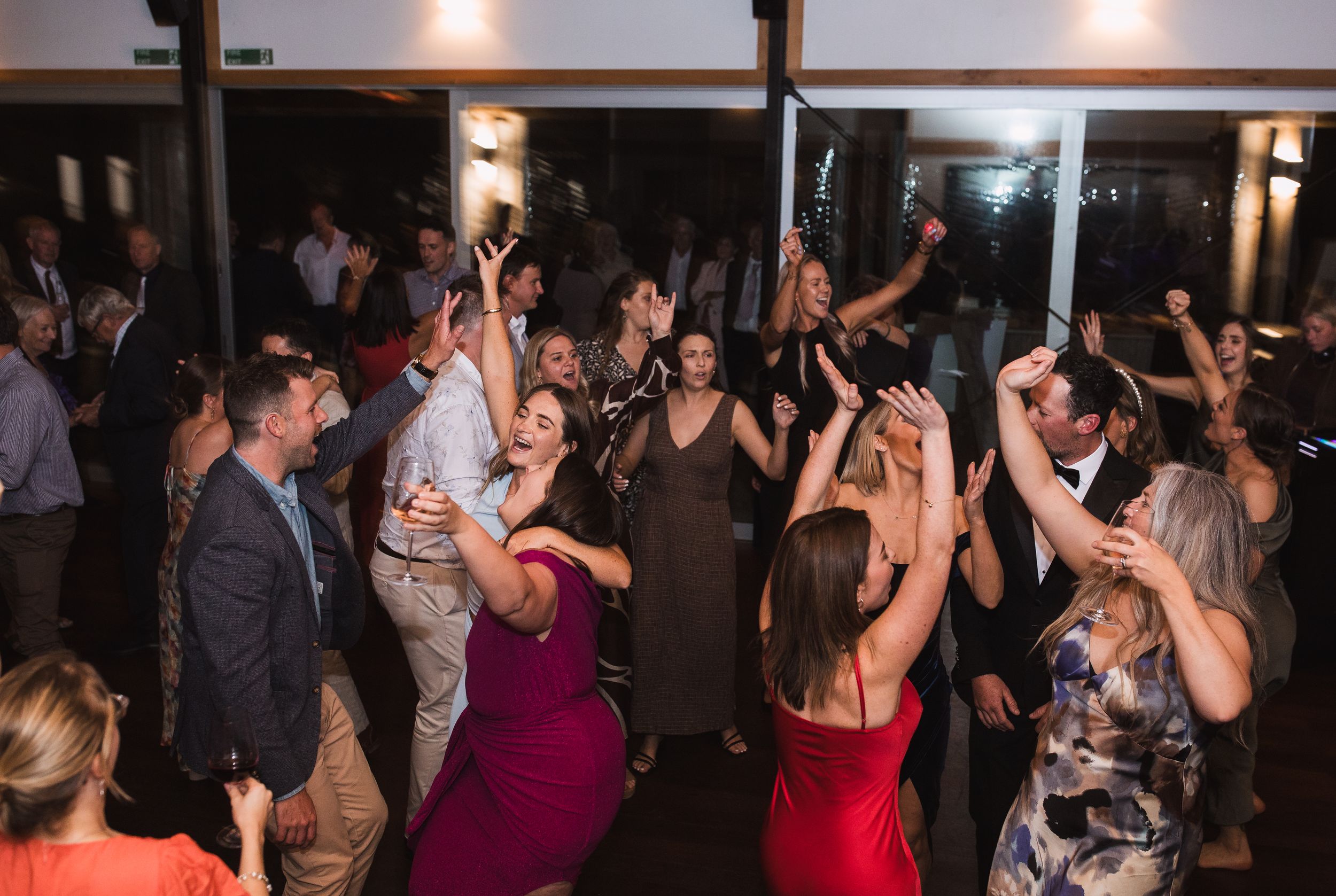 Wedding guests dancing and celebrating on a dimly lit dance floor at an evening reception.