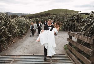Scenic outdoor wedding photos captured on a rustic wooden walkway surrounded by tall grass and rolling hills.
