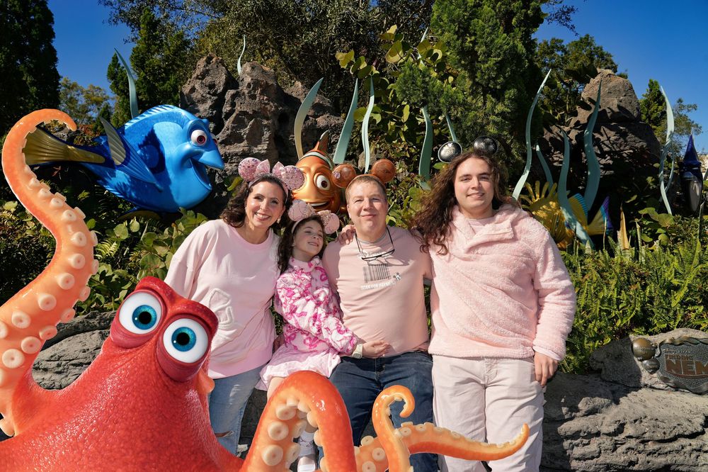 A group of people celebrating outdoors with pink powder during a color festival event on a sunny day.