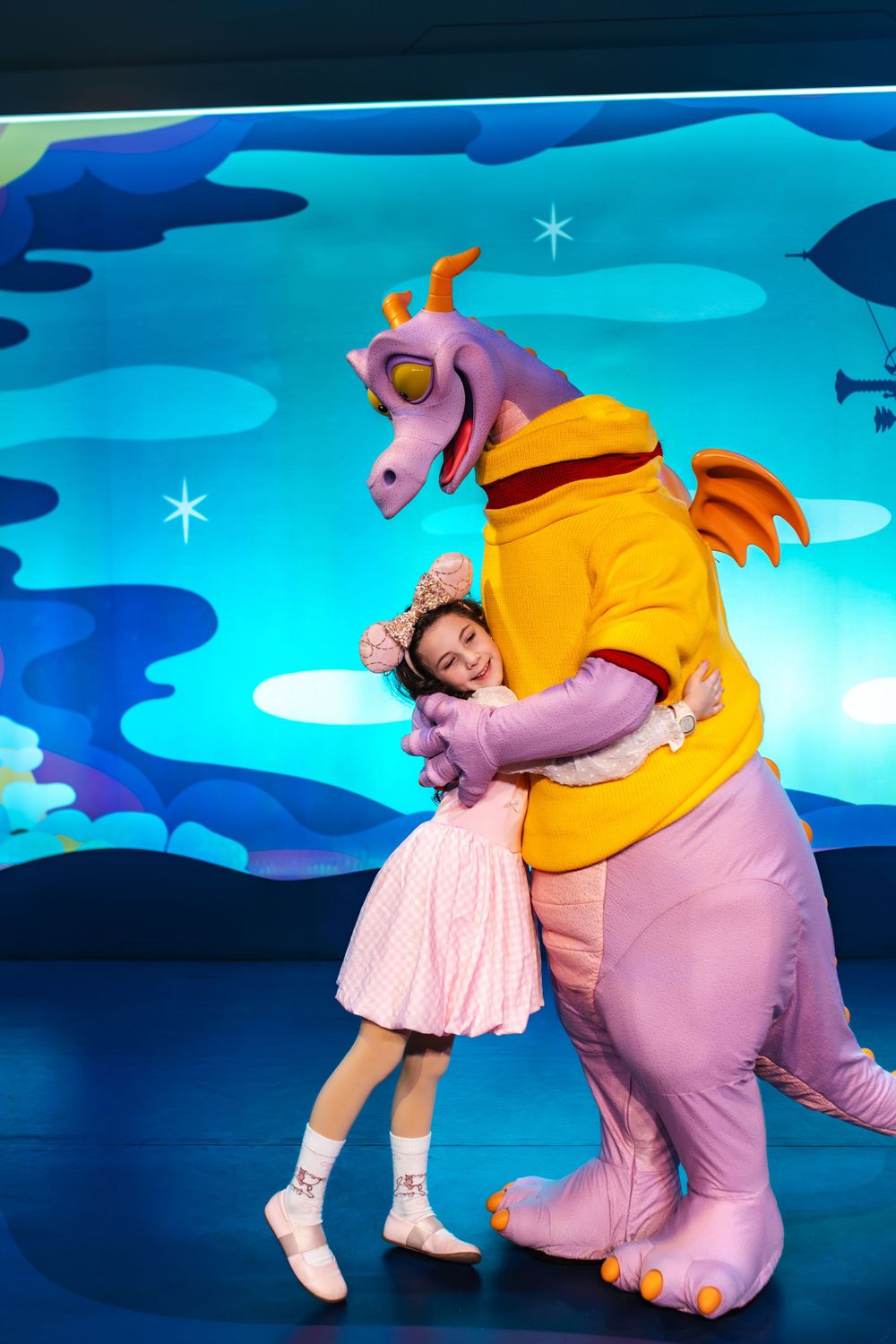 Performers in a children's theater production wearing colorful costumes dance and play together on a blue-lit stage.