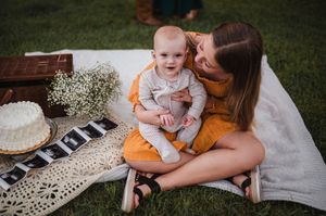 A picnic scene with a blanket, baby's breath flowers and cake on a grassy lawn during a sunny afternoon.