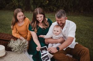 Family in coordinating autumn outfits sits together on grass while looking at mobile phone.