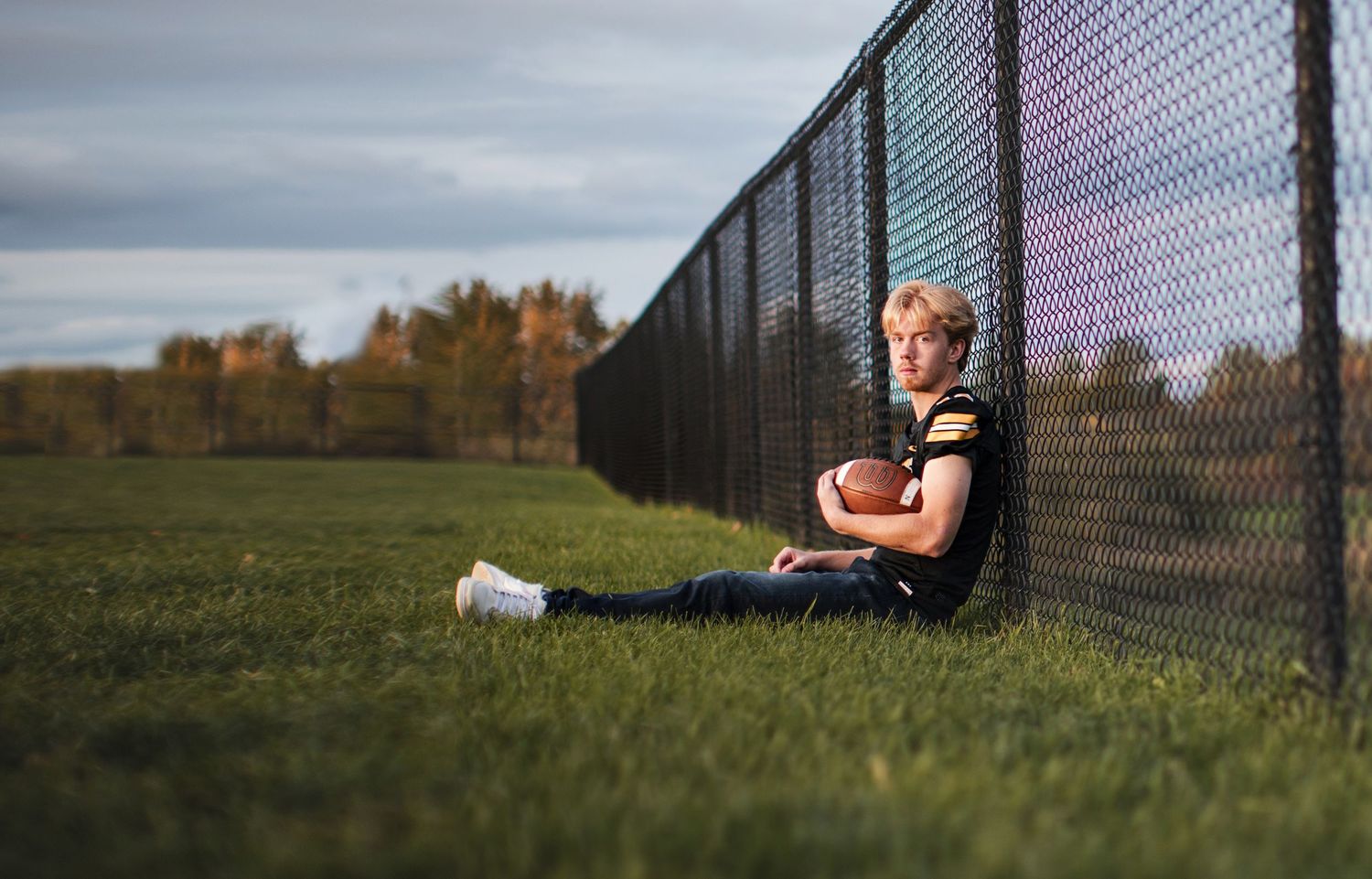 A series of five images showing a person practicing tennis serves against a chain link fence on a grassy field.