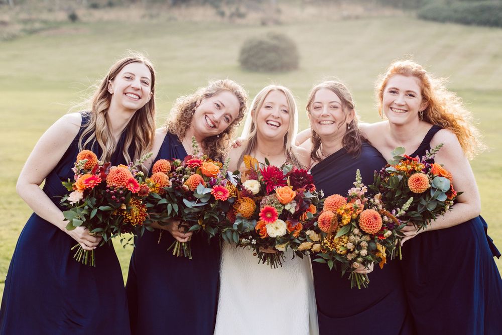 Group holding vibrant autumn-colored floral bouquets with orange and burgundy blooms against a blurred outdoor backdrop.
