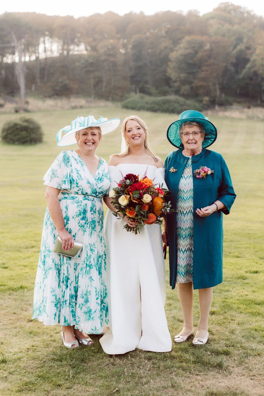 Wedding party members in turquoise dresses and white gown pose together on grassy field at sunset.