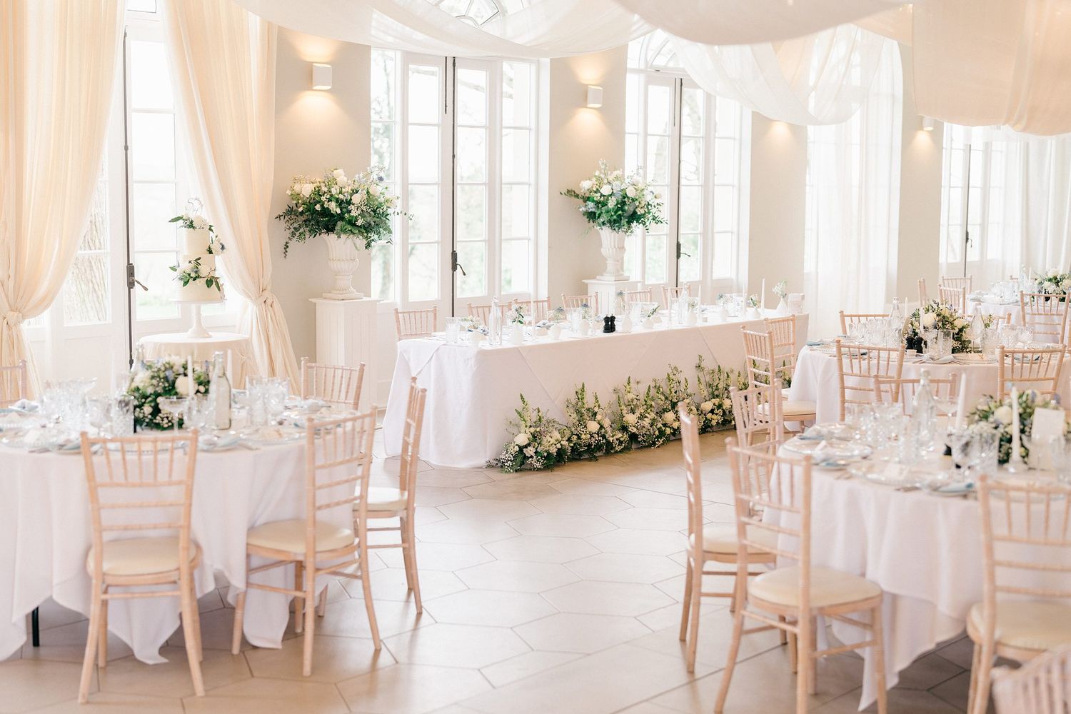 Elegant white wedding reception venue with round tables, chiavari chairs and floral centerpiece arrangements.