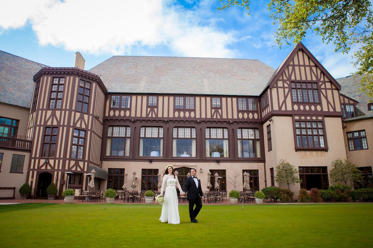 Panoramic view of a Tudor-style wedding venue with multiple buildings and landscaped grounds under blue skies.