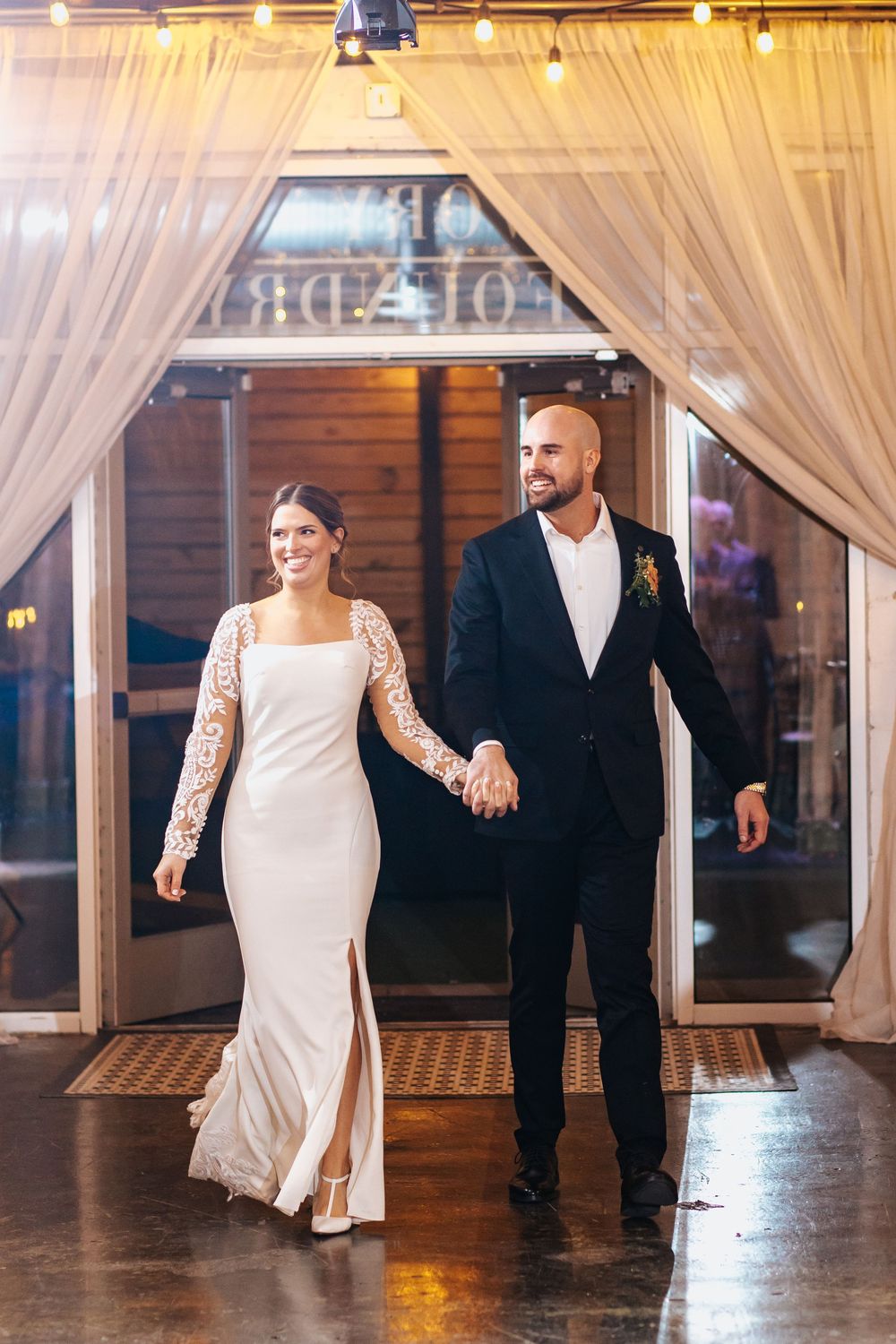 Couple dances together in an elegant venue with white drapes and wooden floors.