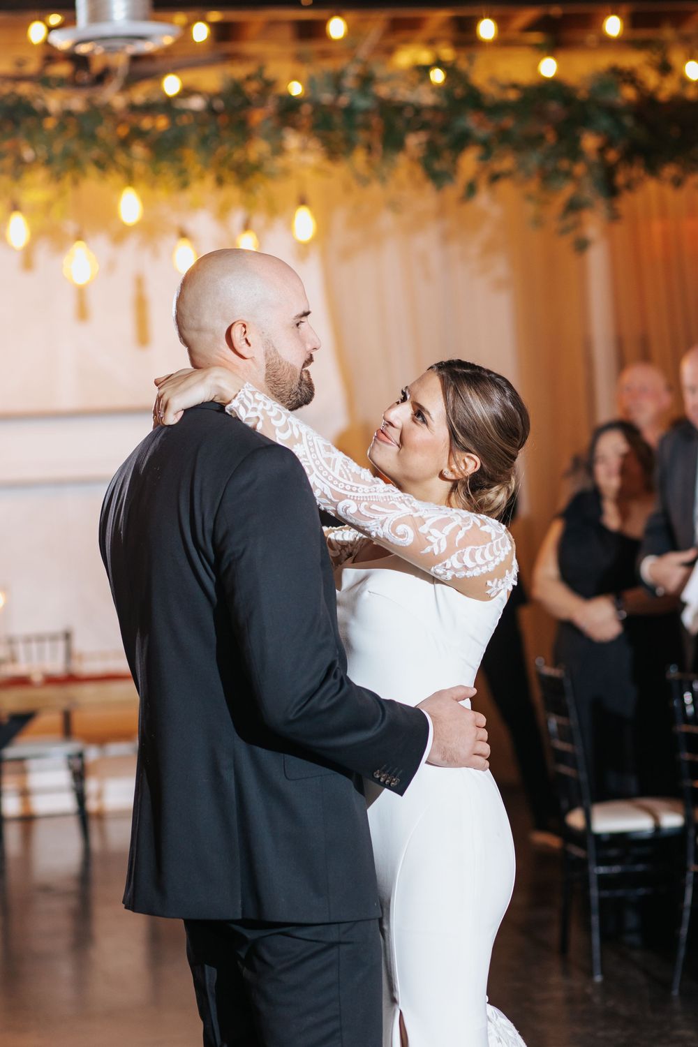 Romantic first dance moment captured in a warmly lit reception venue with string lights.