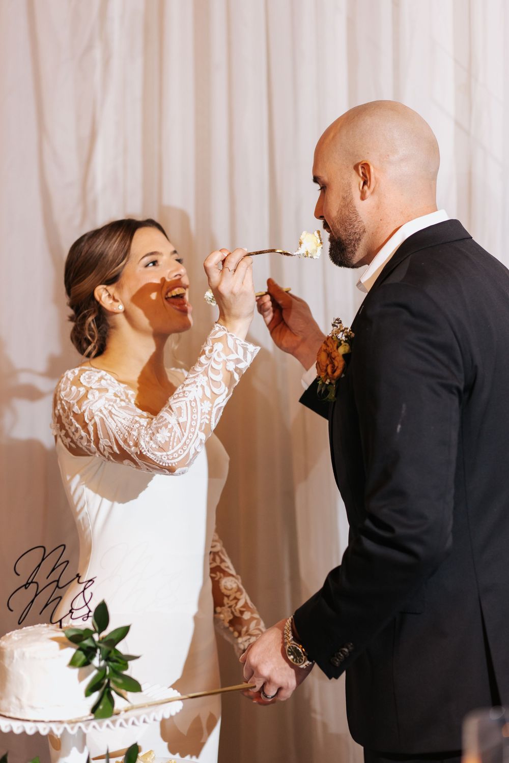 Playful cake feeding moment during wedding reception against white backdrop.