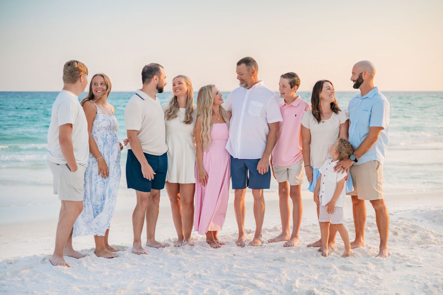 Large extended family of ten holding hands in a line on the beach during a colorful sunset photo session.