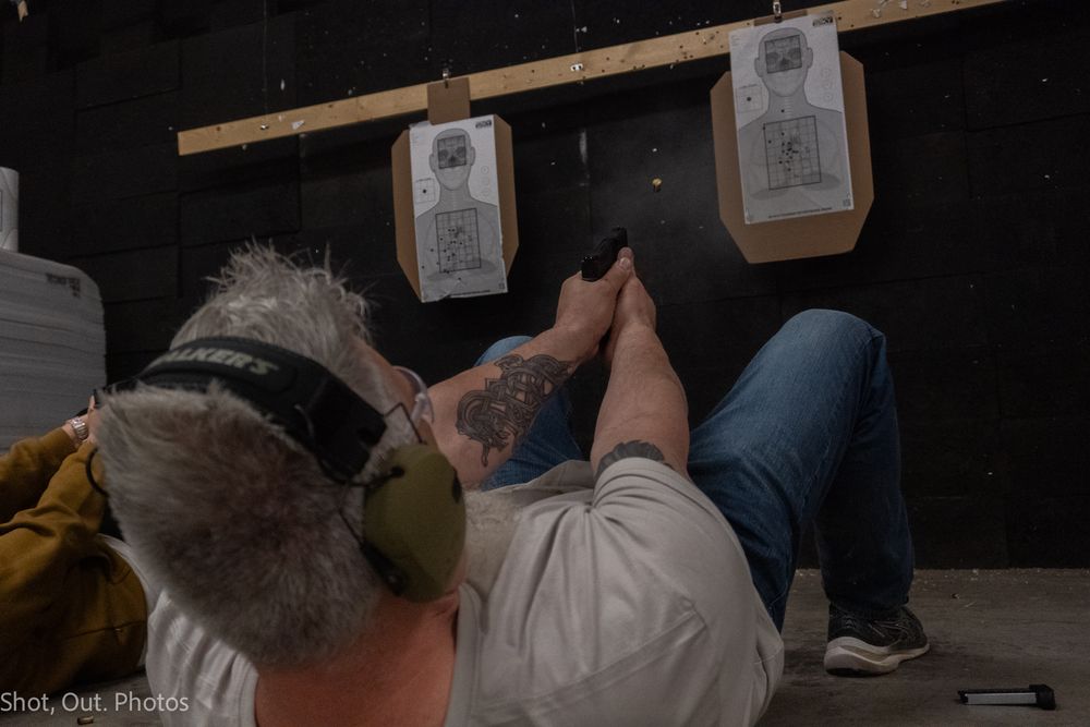 People standing in a line against a dark wall with paper targets visible in the background.