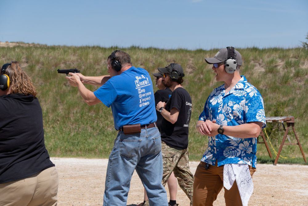 People practicing shooting at an outdoor gun range, wearing ear protection on a sunny day.