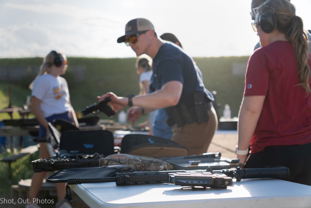 People practicing shooting at an outdoor gun range with rifles while receiving instruction and supervision.