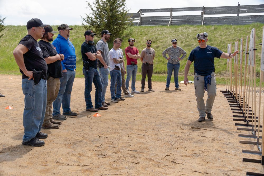 Instructor teaching a group of men firearm safety techniques at an outdoor shooting range training course.
