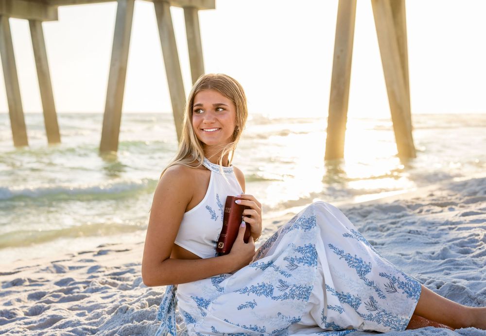 Person relaxing on beach blanket under pier with iced coffee during golden sunset hour.