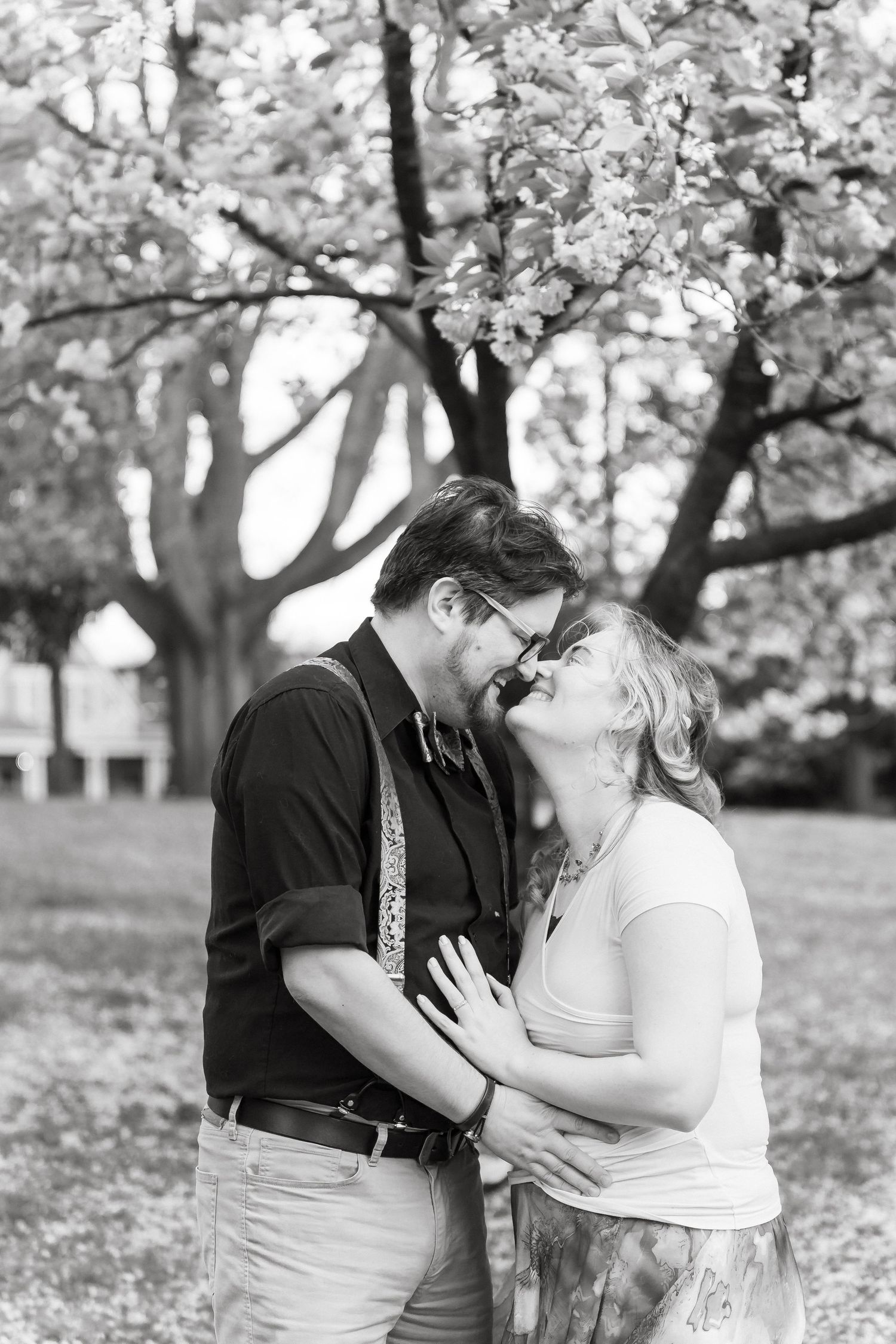 A romantic couple shares tender kisses under blooming cherry blossom trees in a springtime garden setting.