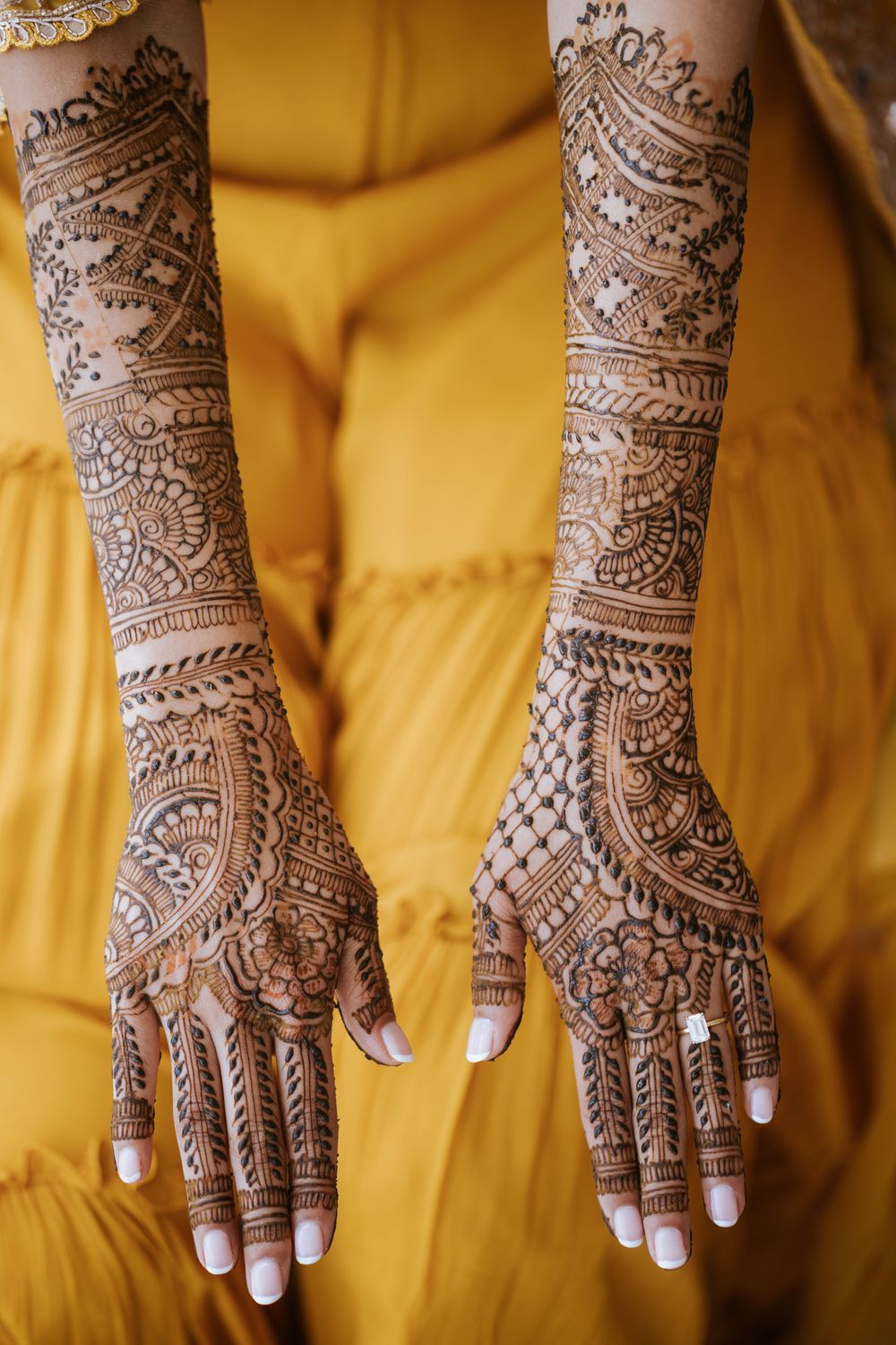 Close-up view of traditional Indian bridal mehndi henna designs on hands against yellow background.