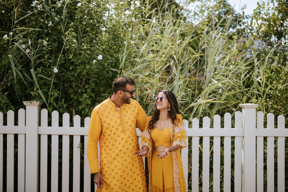 A couple in matching yellow outfits share a romantic moment in front of a white picket fence.