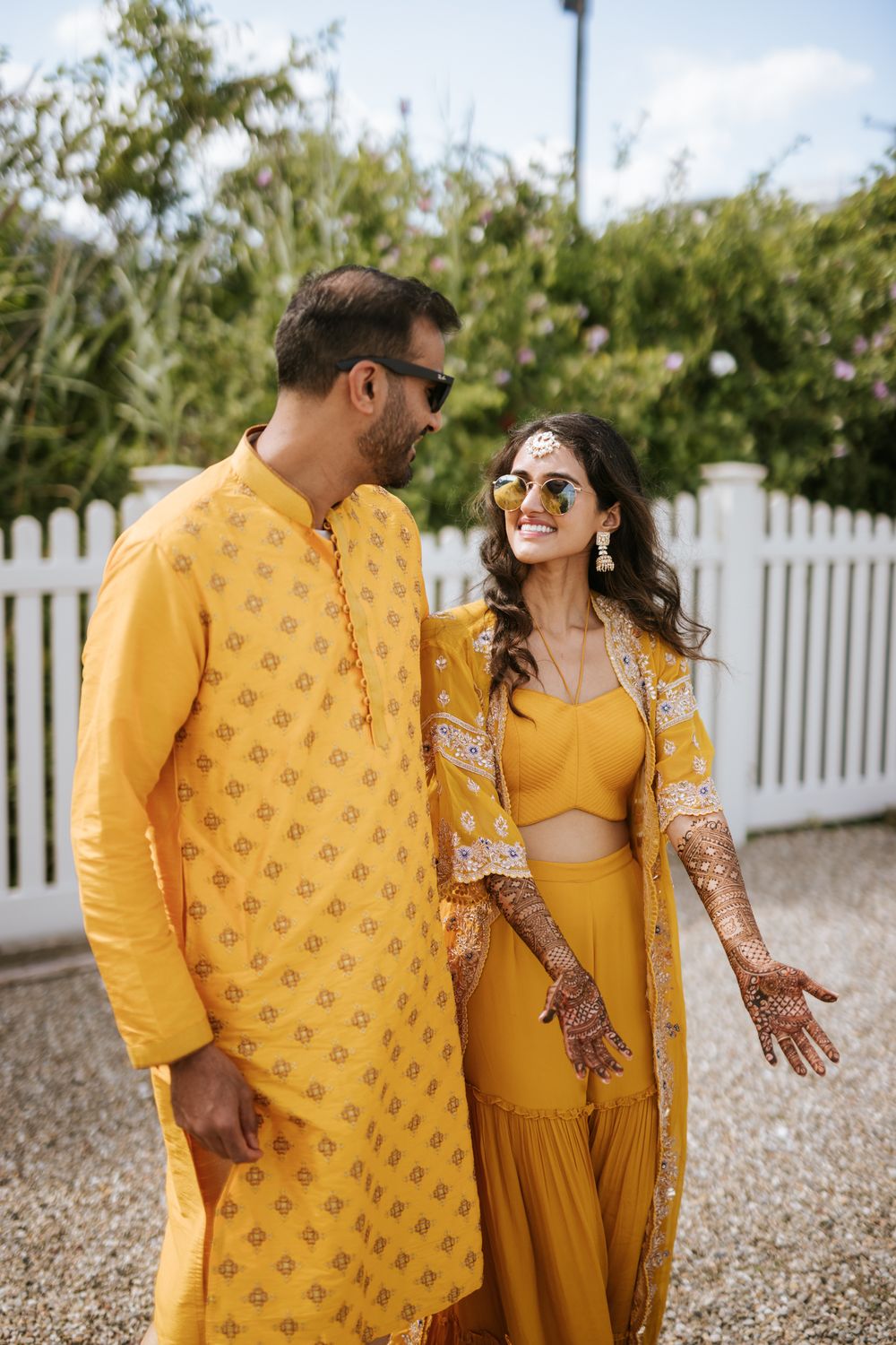A couple in matching yellow traditional Indian outfits share intimate moments together in a garden setting.