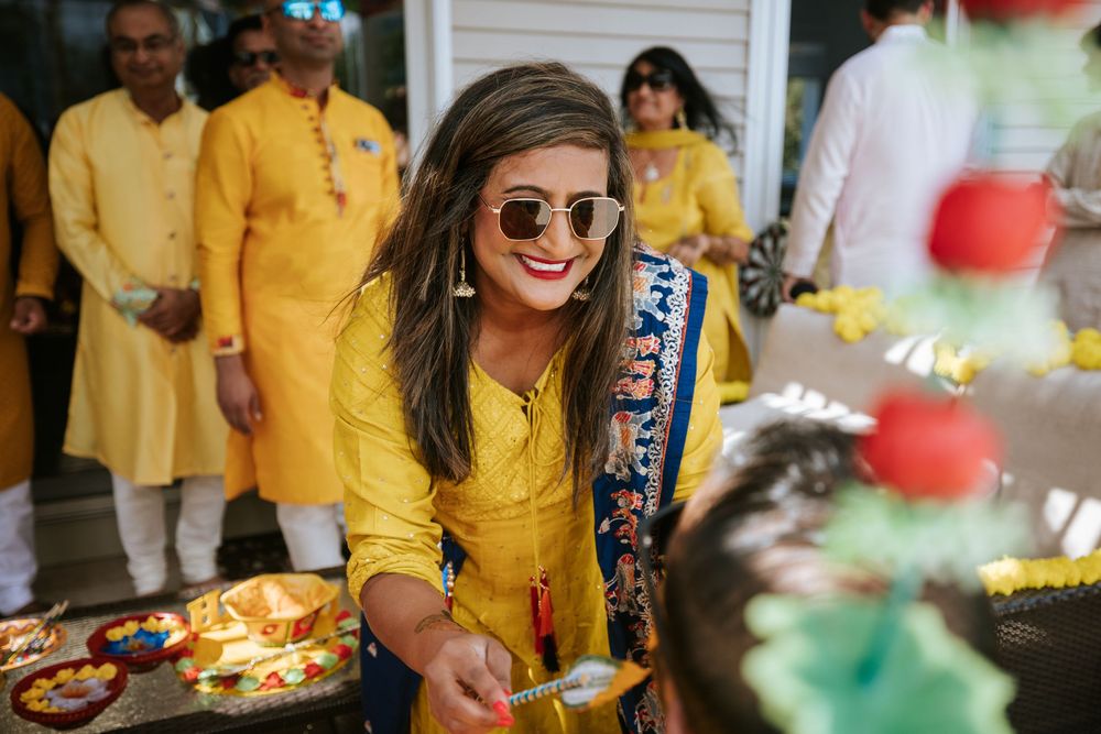 A person in a bright yellow outfit and sunglasses smiles while celebrating at a festive gathering with traditional decor.