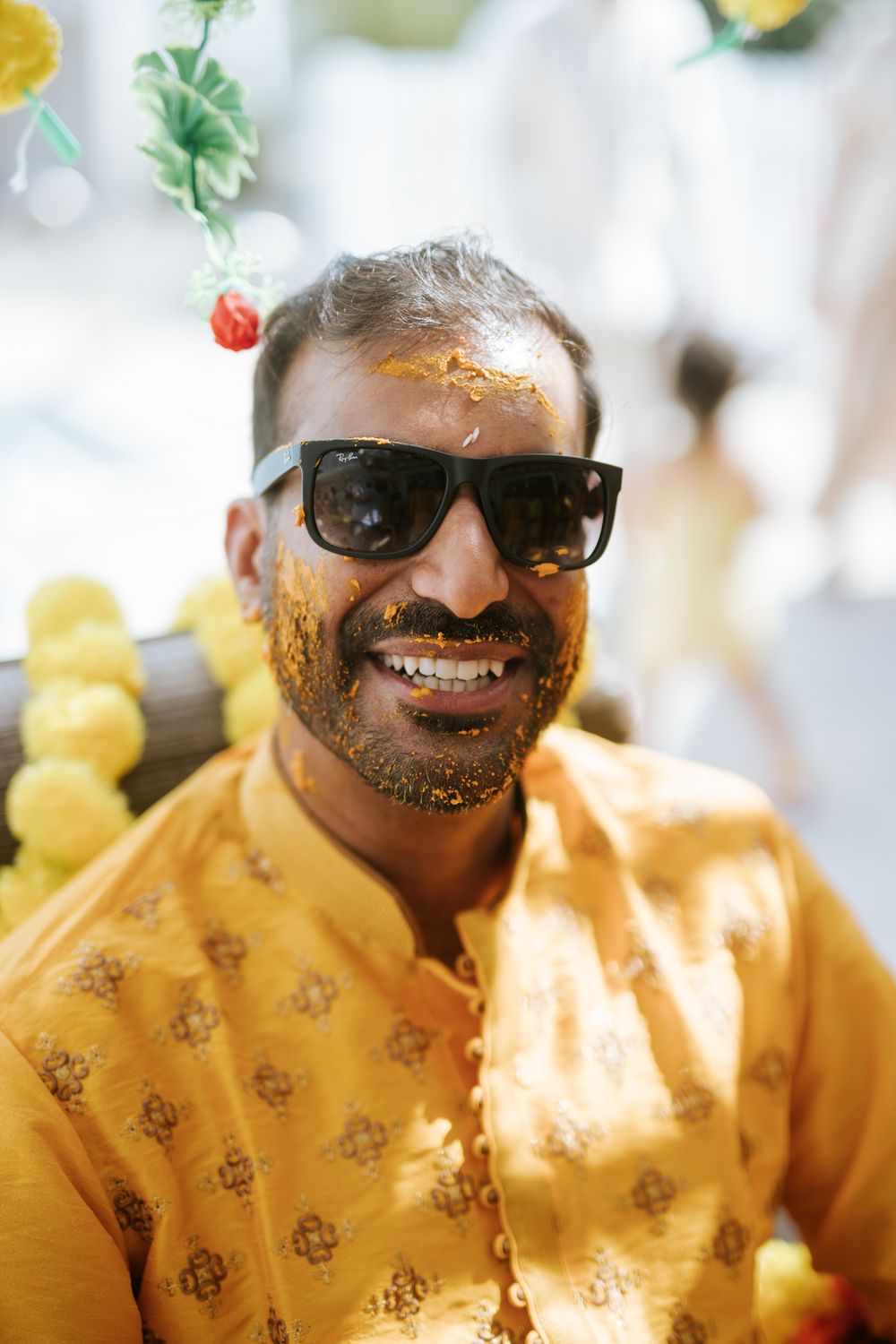 Person wearing yellow patterned shirt and sunglasses smiles in bright natural lighting.