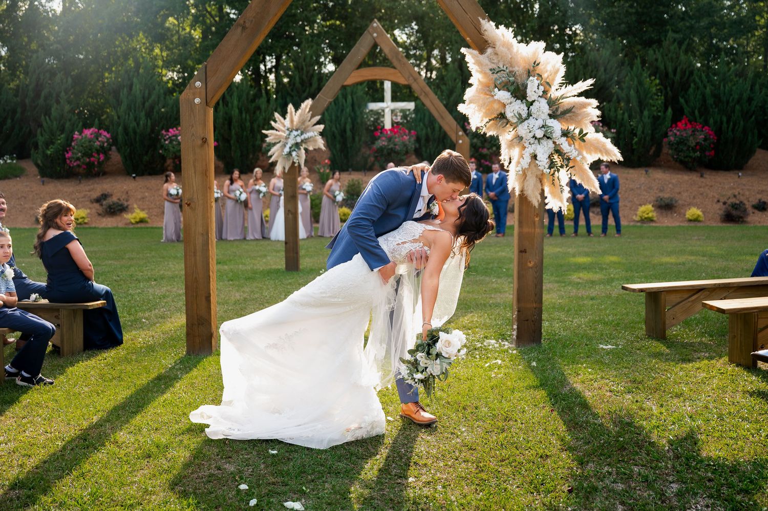 Rustic wooden arch decorated with white flowers stands in an outdoor wedding ceremony setting.