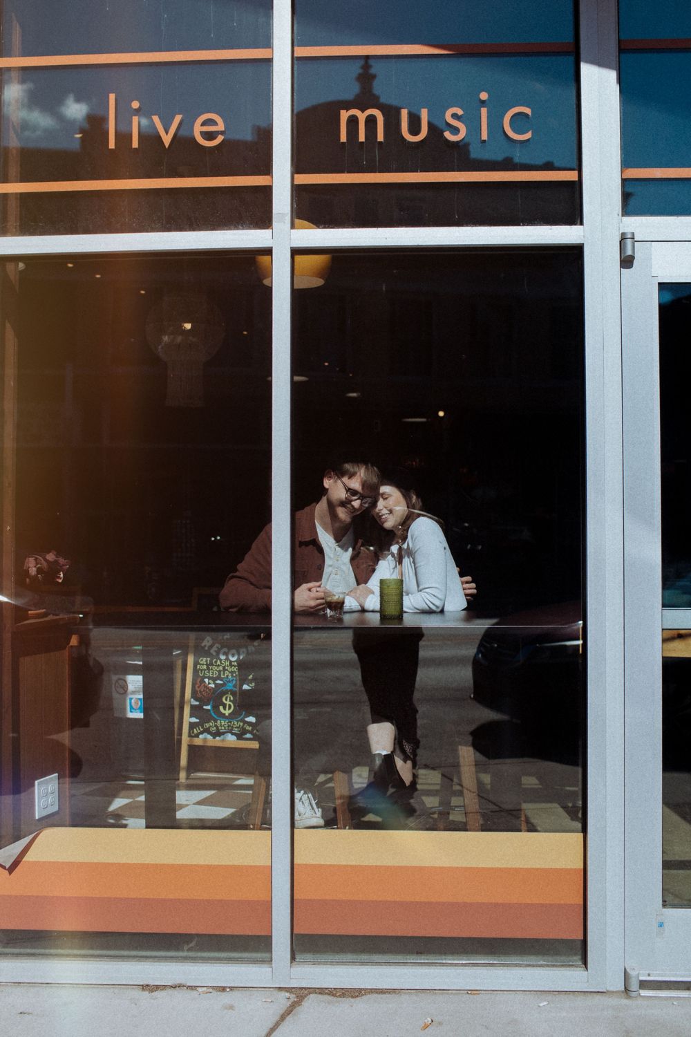 Through a storefront window, a view of a bar or restaurant with 'live music' signage visible in the reflection. Indianapolis, Indiana