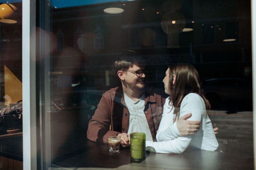 People sitting at a cafe counter with beverages in front of large windows during daytime. Indianapolis, Indiana engagement session.